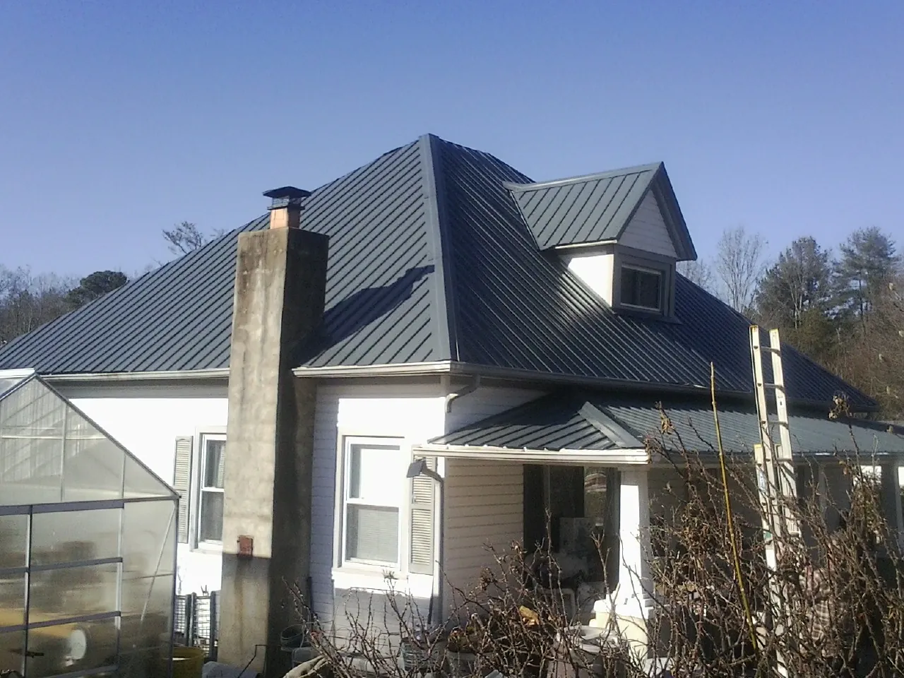 Dark blue standing seam metal roof on a white farmhouse with dormer — Slate & Tile Roof Repair by Roofing Brothers in Chappells