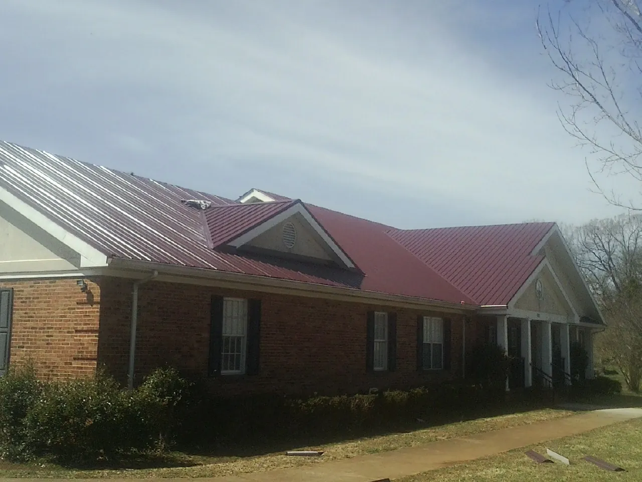 Red metal roof with gabled entries on a long brick building, from a Hail Damage Roof Repair job in Chappells