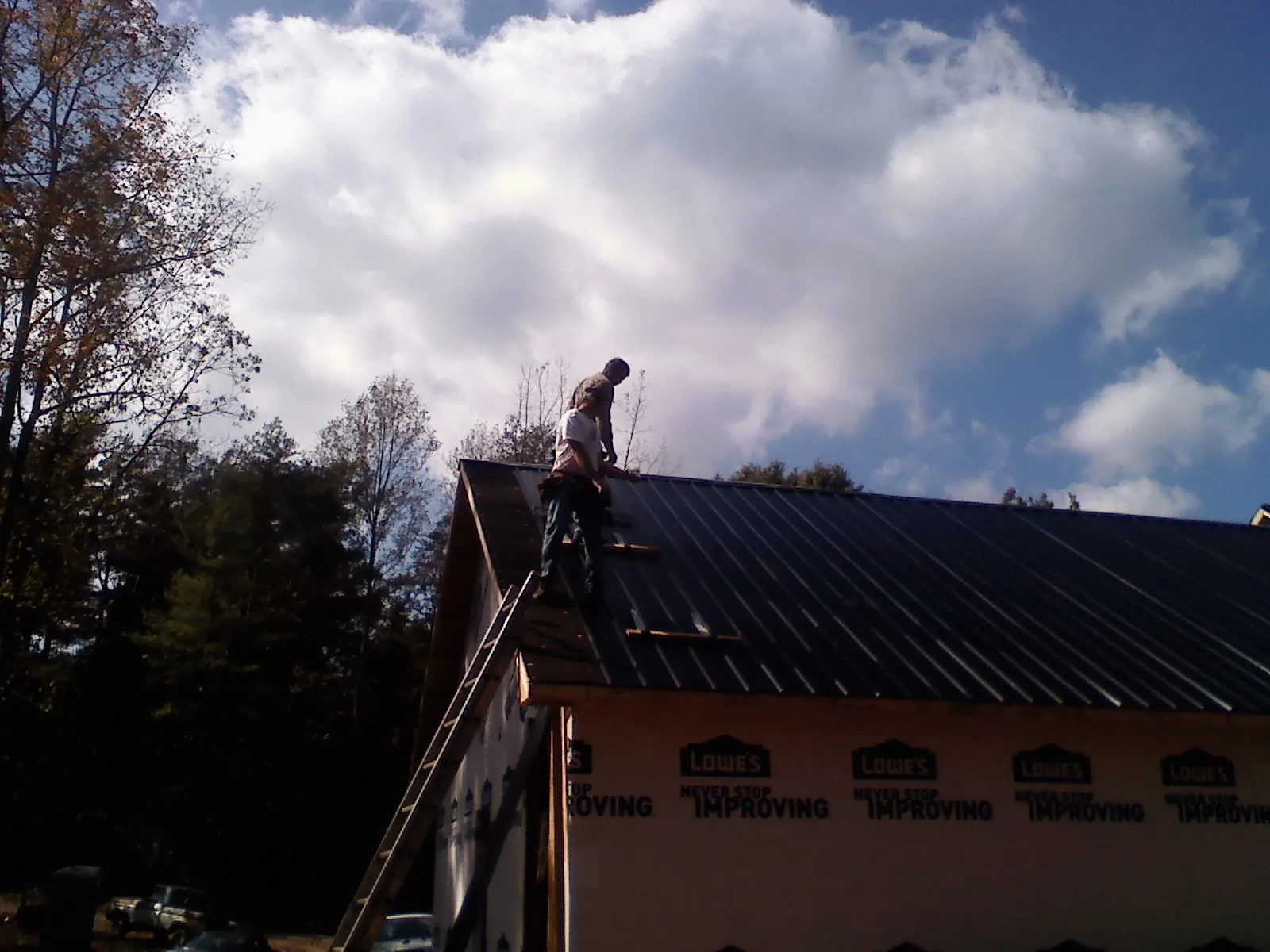 Roofer fastening dark metal panels high against a cloudy sky, from a Roof Inspection job in Chappells